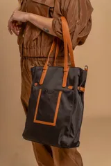 Bolso tipo tote bag de símil cuero color rosa pálido, con asas dobles y detalles de costura en color beige claro. Presenta un bolsillo frontal rectangular aplicado y herrajes metálicos.