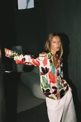 Camisa satinada de manga larga con cuello solapa y cierre frontal con botones, con un colorido estampado floral de estilo acuarela sobre fondo beige.