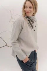 Polera tejida en lambswool color beige, con cuello alto y diseño de intarsia en tonos marrones y grises. Presenta botones forrados en el cuello para modular la apertura.