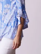 Blusa color salmón con estampado floral blanco, cuello redondo con abertura y mangas 3/4 acampanadas.
