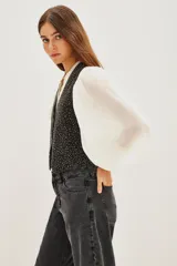 Chaleco de algodón negro con diseño de chaleco de vestir, cuello en V y cierre frontal con botones. La tela está completamente adornada con pequeños apliques brillantes que simulan un efecto de estrellas o puntos de luz.