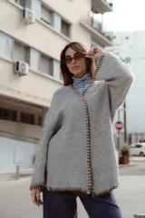 Saco oversize de tejido de punto en color gris, con mangas caídas y bordados artesanales en los bordes en tonos tierra y violeta.