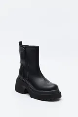 Bota de caña media color negro, con plataforma robusta y suela dentada. Presenta un diseño minimalista con cierre lateral para un calce práctico.