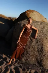 Vestido midi de gamuza color marrón cognac, con escote en V y detalles de calados geométricos artesanales en rombos. Presenta costuras decorativas con ribetes de cuero metalizado en tono cobre.