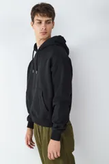 Buzo con capucha de color negro, con bolsillo tipo canguro frontal, mangas largas con puños elásticos y cordones ajustables en el cuello.