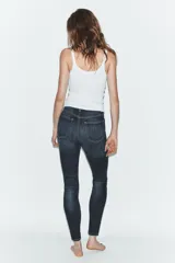 Jeans de tiro alto con corte skinny y largo tobillero. Presenta diseño clásico de cinco bolsillos, cierre frontal con cremallera y botón, con un acabado de lavado azul medio.