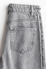 Jean de tiro alto, corte ancho y pierna recta, confeccionado en denim de algodón rígido color gris lavado. Presenta una franja lateral negra contrastante con acabado desflecado en los bordes.