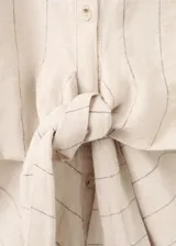 Camisa de lino y algodón color beige con estampado de raya diplomática, cuello camisero, manga corta y detalle de nudo en la cintura con cierre delantero de botones.