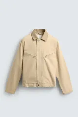 Cazadora relaxed fit de Zara confeccionada en denim de algodón color beige, con cuello de solapa en piel combinada, bolsillos con cremallera en el pecho y cierre frontal oculto.