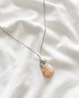 Collar con cadena plateada y dije de piedra color naranja.