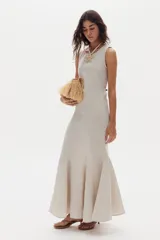 Vestido largo de lino color beige, sin mangas, con cuello redondo y diseño ajustado que se ensancha en la parte inferior con godets que aportan movimiento al ruedo.