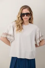 Remera de algodón color blanco, con cuello redondo y mangas cortas holgadas que presentan detalles de encaje broderie.