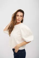 Camisa de algodón color blanco, con cuello redondo, cierre frontal oculto y mangas abullonadas de largo tres cuartos.