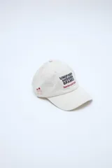 Gorra clásica color beige con bordado frontal en negro y rojo con el texto "Uniform Hidden Sparks Stories with Style", y bordado lateral de montañas.