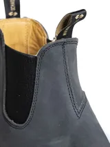 Bota tipo Chelsea de cuero color gris oscuro, con elásticos laterales negros y suela de goma dentada. Presenta tiradores en la parte superior para facilitar el calce.