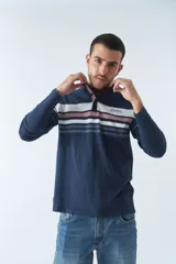 Remera tipo polo de manga larga azul marino con rayas horizontales blancas, grises y rosadas en el pecho. Tiene cuello clásico con botones y logo estampado en el pecho. Corte regular.