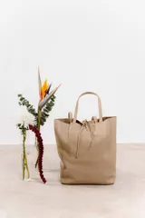 Bolso tote confeccionado en cuero legítimo color beige. Diseño minimalista con cierre superior mediante tira de cuero y doble asa corta.