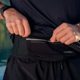 Riñonera deportiva minimalista marca Merrell, color negro, diseñada para trail running. Cuenta con cierre frontal, ajuste elástico y múltiples bolsillos para almacenamiento ligero.