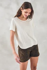 Remera color crudo de algodón peinado, de corte recto y mangas cortas. Presenta cuello redondo con detalle de cadena metálica dorada.