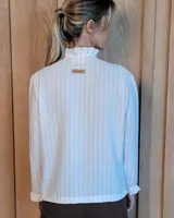 Camisa de manga larga con estampado de rayas verticales en tonos crudo y beige. Presenta cuello alto con volados, cierre frontal con botones dobles y puños con volados.