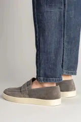 Zapatillas tipo mocasín de gamuza gris plomo con suela blanca de goma y detalle de antifaz en el empeine.