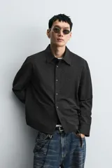 Camisa negra de corte relaxed fit, con cuello solapa y cierre frontal de botones, manga larga con puños abotonados y sutil patrón geométrico en jacquard.