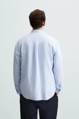 Camisa celeste a rayas verticales, de corte relaxed fit, confeccionada en lino y algodón. Tiene cuello abotonado, manga larga con puños abotonados, bolsillo de parche en el pecho y cierre frontal con botones.