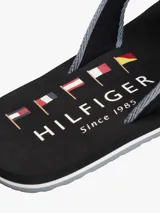 Ojotas Tommy Hilfiger negras con tira de tela trenzada azul y logo de la marca en la tira.