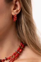 Aros tipo argolla pequeña de acero quirúrgico, decorados con mostacillas entrelazadas en tonos rojizos y detalles metálicos.