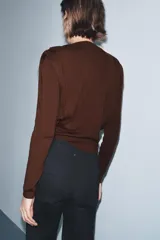 Jersey de punto color marrón oscuro, con cuello redondo, manga larga y hombreras con pliegues.