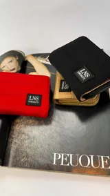 Billetera corta de diseño capitoneado con cierre perimetral y tapa frontal. Incluye compartimentos internos para tarjetas y billetes, y cuenta con una correa de mano desmontable. Presenta un parche con el logo de la marca LNS Lincoln's.
