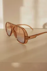 Lentes de sol estilo aviador con armazón de policarbonato en tono ámbar translúcido y cristales degradados.