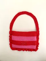 Cartera tipo shoulder bag tejida a crochet en hilo de algodón, con diseño a rayas en tonos de rojo y rosado, y detalles de volados en los bordes y la manija de hombro.