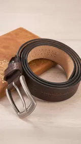 Cinto de cuero marrón con diseño de doble costura decorativa y perforaciones a lo largo de la tira. Cuenta con hebilla metálica de acabado mate.