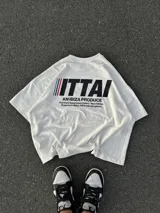 Remera marrón de corte holgado con estampado en la espalda que incluye la palabra "ITTAI" en blanco con líneas rojas y azules, la frase "AN IBIZA PRODUCE" y un texto más pequeño que dice "Ittai Stars Department Gallery - Ibiza Edition. If you're in Ibiza, 112 is not an option.".