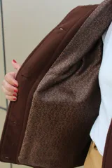 Campera de paño de lana en color beige jaspeado, con diseño oversize. Presenta detalles en pana color marrón chocolate en los puños y en las tapas de los bolsillos frontales. Cuenta con cierre frontal de botones grandes y cuello alto.