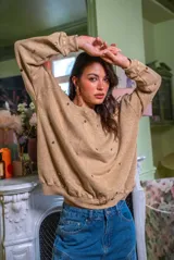 Sweater de corte oversize color beige, confeccionado en algodón. Presenta un diseño holgado con cuello redondo, puños y ruedo acanalados, decorado con múltiples apliques metálicos circulares en tonos dorados y plateados distribuidos por toda la prenda.