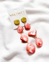 Aros colgantes con base de círculo dorado y tres piedras nacaradas en tonos rosados y blancos, unidas por argollas doradas.