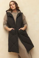 Chaleco largo negro capitoneado con capucha, dos bolsillos laterales, doble cierre y forro interno de satén con estampado animal print.