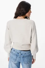 Sweater de punto color crudo con cuello redondo, mangas largas con puños anchos acanalados y cintura también acanalada. Presenta un diseño de silueta holgada y mangas con volumen.