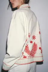 Sobrecamisa color crudo de Zara Woman Collection, con cuello solapa y manga larga. Tiene bolsillos de parche en el delantero y bordados combinados a contraste en color rojo. Cierre frontal con botones a presión ocultos.
