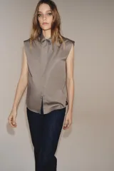 Camisa sin mangas confeccionada en algodón, con cuello redondo y detalle de lazada frontal. Presenta cierre frontal con botones ocultos por solapa y bajo redondeado.