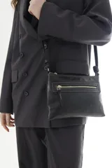 Bandolera de cuero negro, de diseño rectangular y compacto, con correa ajustable para llevar cruzada al hombro. Cuenta con un bolsillo frontal con cierre y detalles de costuras pespuntadas a contratono.