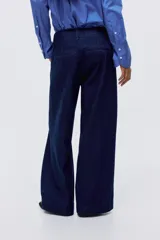 Pantalón de jean tipo wide leg de tiro alto, confeccionado en denim rígido de color azul oscuro. Presenta un corte holgado desde el muslo hasta el ruedo, con raya marcada en el centro de las piernas, cierre con botón oculto y bolsillos al bies.