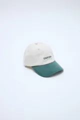 Gorra clásica con diseño en bloque de color, cuerpo en tono beige y visera en verde. Cuenta con bordado frontal con la palabra 'UNIFORM'.