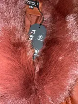 Tapado de cuero sintético color bordó, con cuello y puños de piel sintética desmontables. Presenta cierre frontal con botones y cinturón ajustable con hebilla forrada en el mismo material.