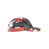 Gorra de béisbol con diseño de camuflaje en tonos rojos, blancos y negros, decorada con múltiples parches bordados que incluyen nombres de ciudades como Manhattan, London, Shibuya y Tokyo, además de la marca Supreme.