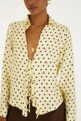Blusa de lunares color amarillo con diseño de puntos y detalles oscuros, cuello camisero y cierre frontal con cordones para atar.