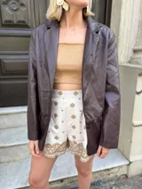 Blazer de cuero sintético en color marrón oscuro, con cierre frontal de dos botones y solapas clásicas.