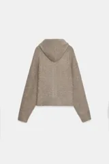 Chaqueta de punto con capucha, manga larga y cierre frontal con cremallera. Presenta un diseño en color beige con un lazo decorativo a contraste en color marrón oscuro en la zona del cuello.